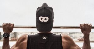 Back view of a man in gym attire doing pull-ups outdoors, demonstrating strength and fitness.