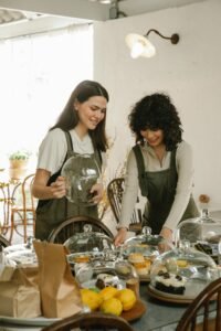 Two women in aprons organizing pastries at a cozy café indoors.